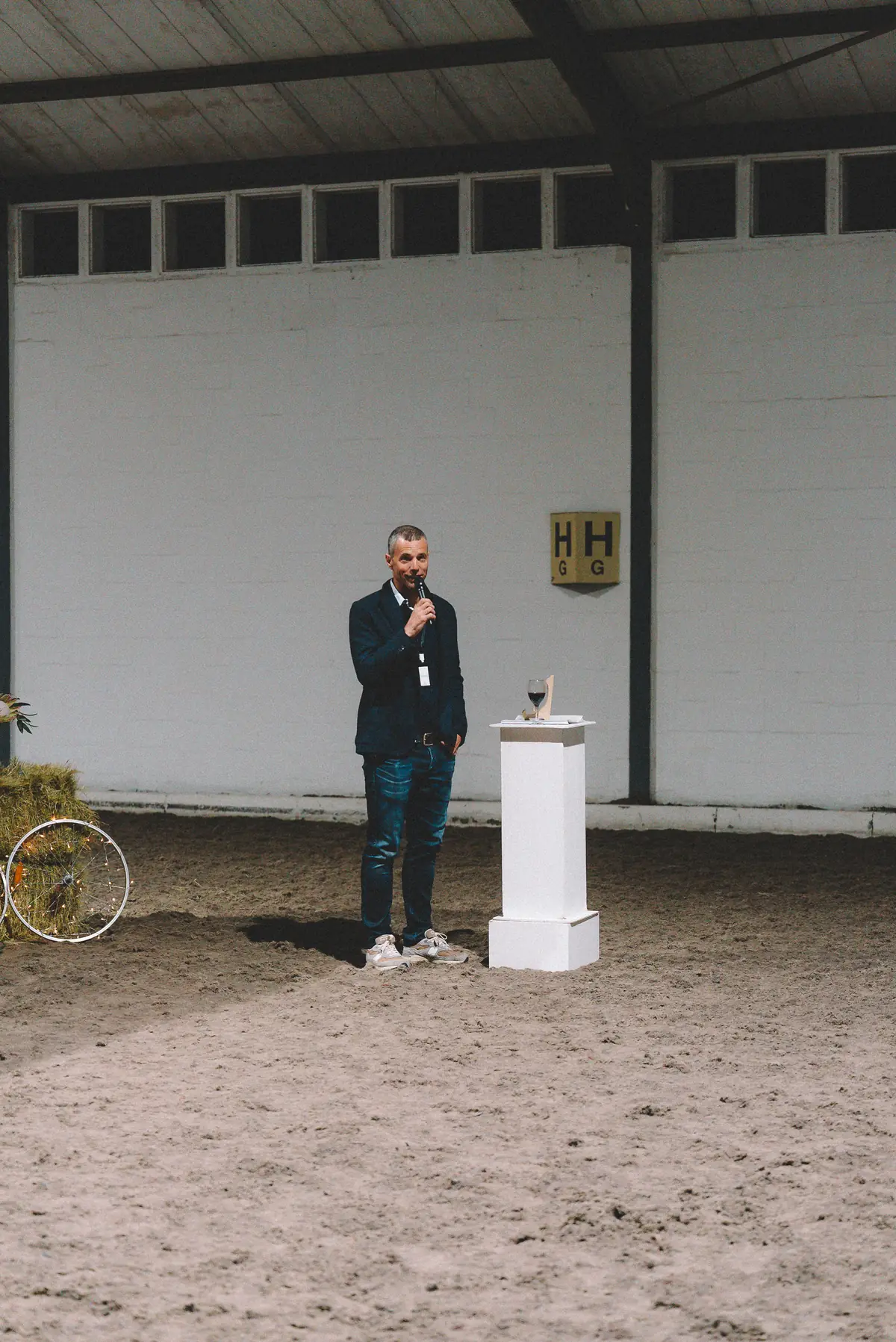 A host speaking into a microphone in the indoor arena at Banhoek Stud, beside a white plinth