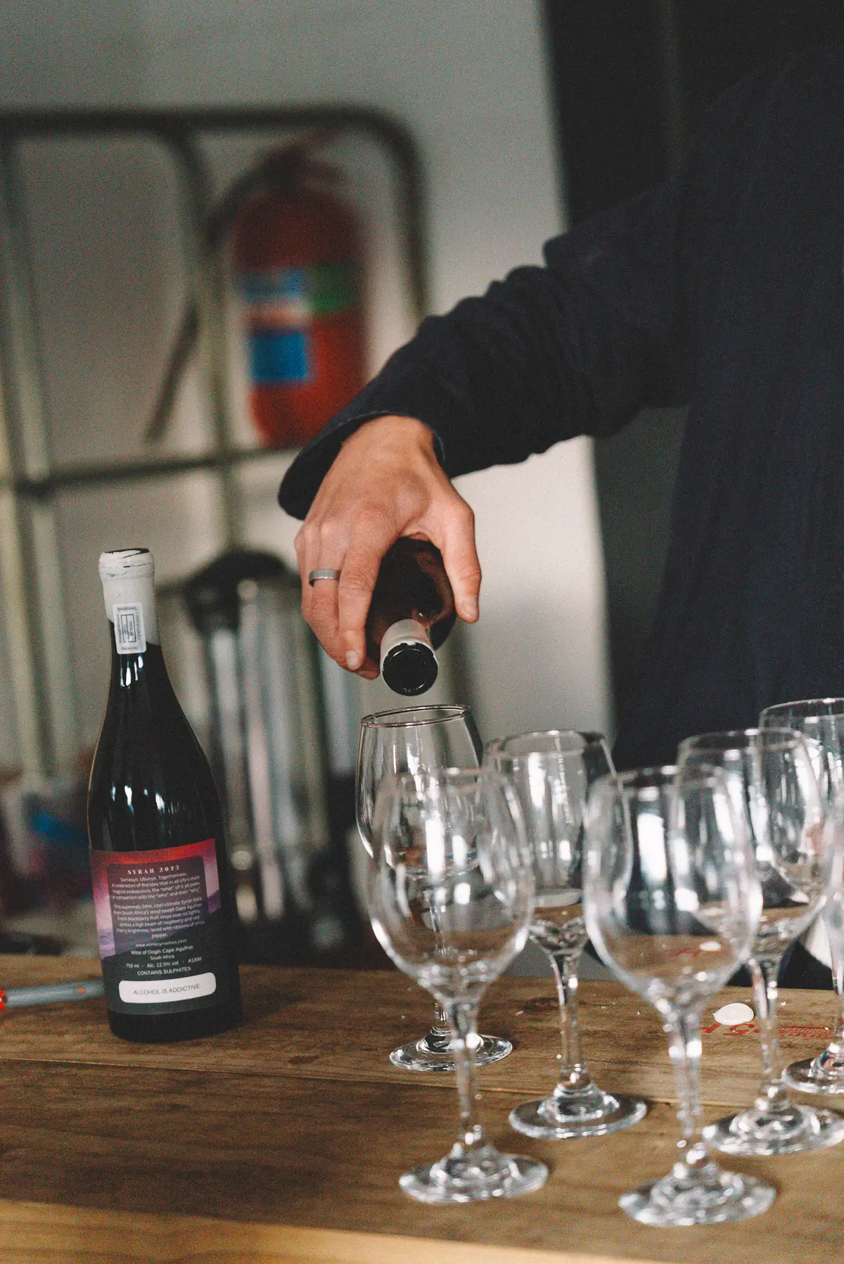 Red wine being poured into a row of glasses on a wooden table at Banhoek Stud