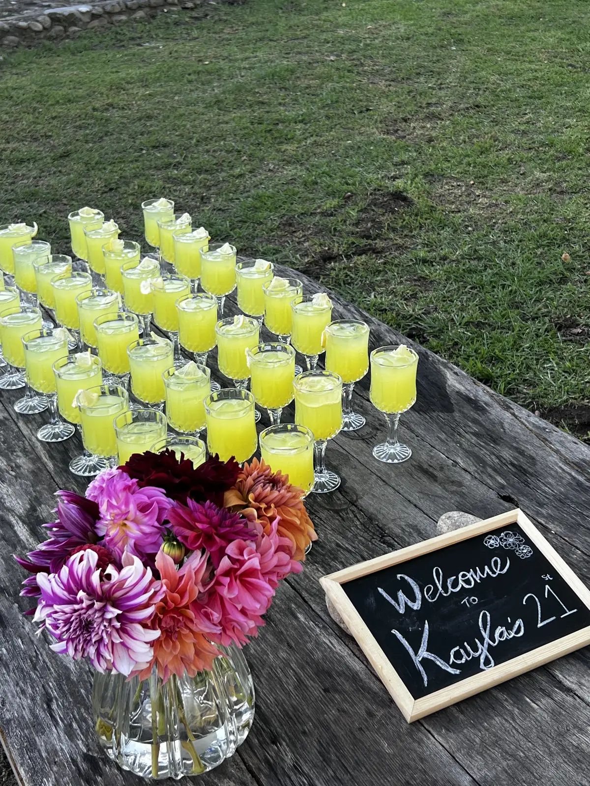 Welcome drinks arranged on a wooden table with fresh dahlias at a private event at Banhoek Stud